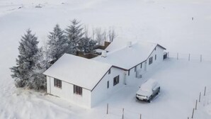 Paisaje nevado con una casa blanca y un auto estacionado adelante.