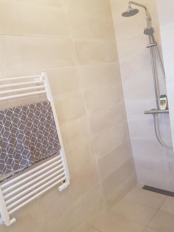 Un baño con ducha, un perchero con una toalla estampada y un radiador.