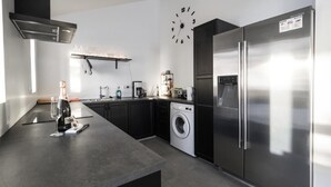 Una cocina moderna con un refrigerador de acero inoxidable, una lavadora y un reloj en la pared.