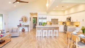 A modern kitchen with a central island, bar stools, and a dining area with wooden chairs. - Ma'alaea Surf, Unit E1-2 BR Ground Floor Beachfront Condo, AC, Wifi, Pool (Kihei)