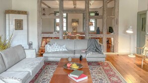 Un salon spacieux avec un canapé gris, une table basse en bois sur laquelle sont posés des livres et des fruits, et un tapis à motifs.