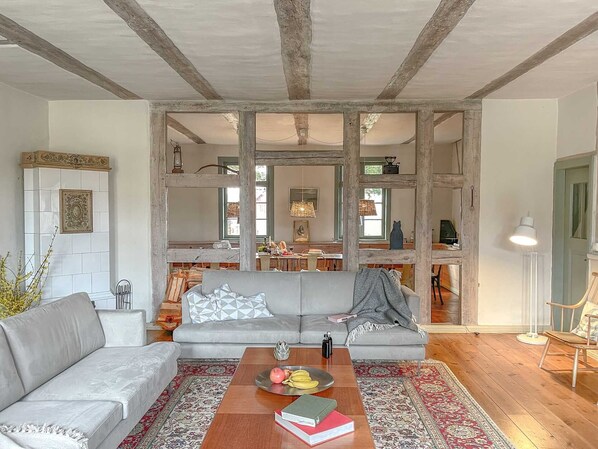 A spacious living room with a grey sofa, a wooden coffee table with books and fruit, and a patterned rug.