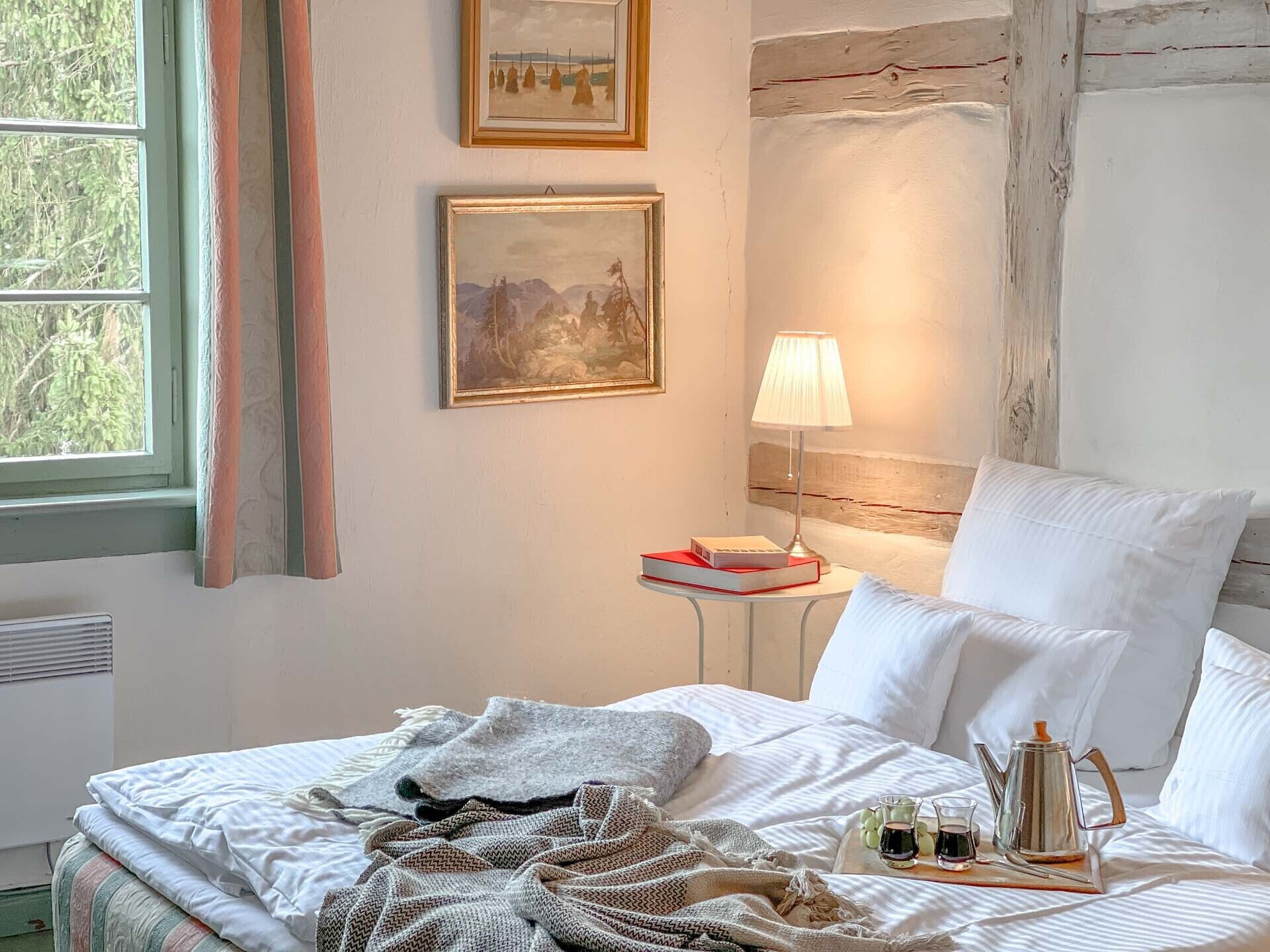 Un lit bien fait, avec des oreillers, une table de chevet avec une lampe et deux tableaux encadrés accrochés au mur.