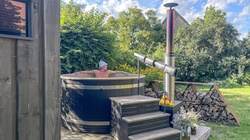 Un bain à remous avec une cheminée, des marches en bois et une pile de bûches.