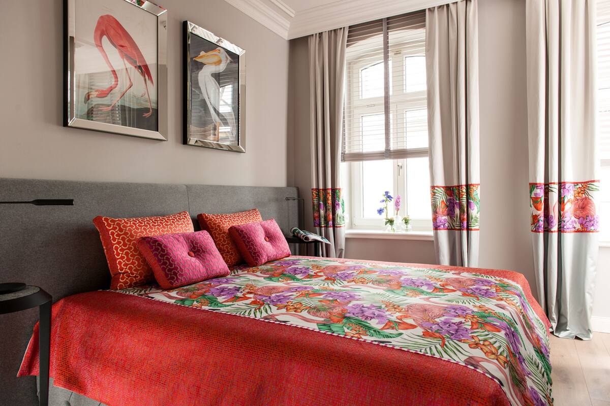 A bedroom with a large bed, a grey headboard, and two framed wall art pieces.