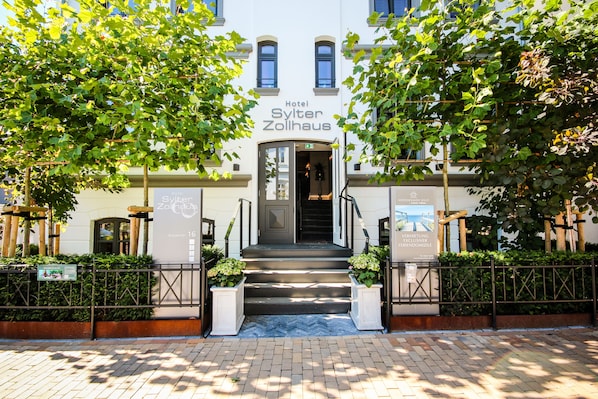 The entrance of Hotel Sylter Zollhaus with a staircase leading up to the door, surrounded by greenery and a brick pathway. - Hotel Sylter Zollhaus (Sylt)