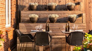 An outdoor dining area with a wooden table and chairs, potted plants, and a brick wall. - Hotel Sylter Zollhaus (Sylt)