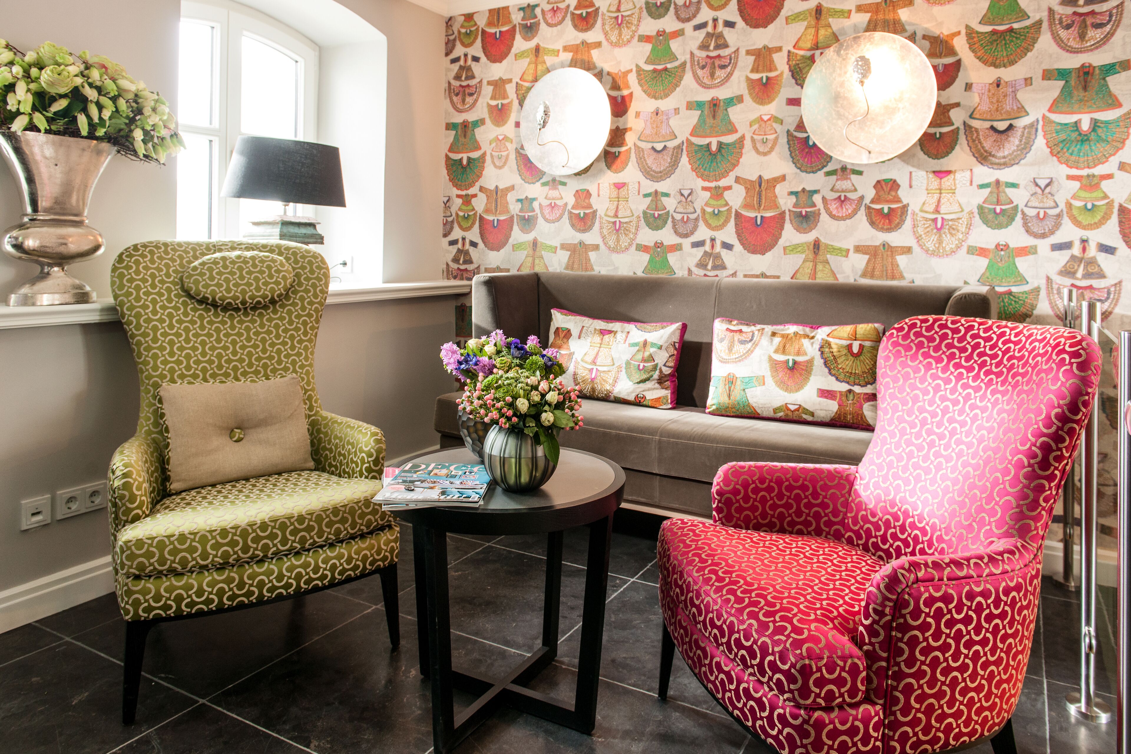 Ein Wohnzimmer mit gemusterten Sesseln, einem runden Couchtisch und einem Sofa mit dekorativen Kissen.