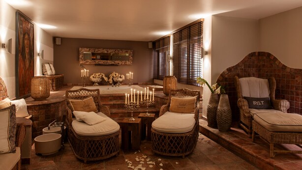 A cozy, well-lit room with wicker furniture, a stone fireplace, and a large mirror on the wall. - Hotel Sylter Zollhaus (Sylt)