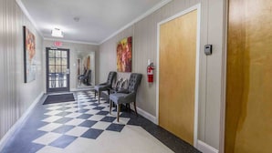 A hallway with a checkered floor, two grey armchairs, a fire extinguisher, and a door with a wooden panel. - 1BR Sparkling Clean Apartment, KING Bed (Winston-Salem)