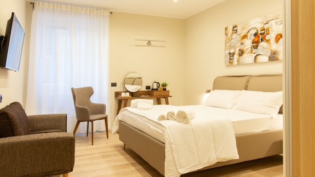 Una habitación de hotel moderna con una cama, una silla, un escritorio con espejo y un cuadro en la pared.
