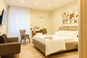 A modern hotel room with a bed, a chair, a desk with a mirror, and a painting on the wall.