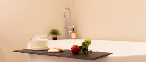A bathroom with a bathtub, a small shelf with a candle, a plant, and a bottle.