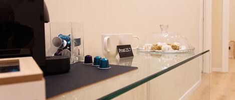 A hotel reception area with a coffee machine, a glass display case with pastries, and a sign indicating room rates.