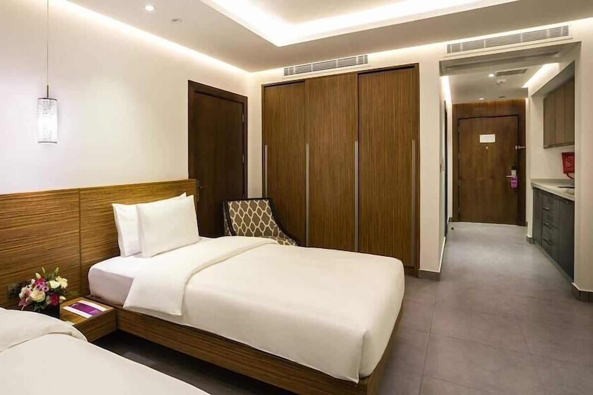 Una habitación de hotel con una cama grande, una mesita de noche con un libro y flores, un armario y un baño visible a través de una puerta abierta.