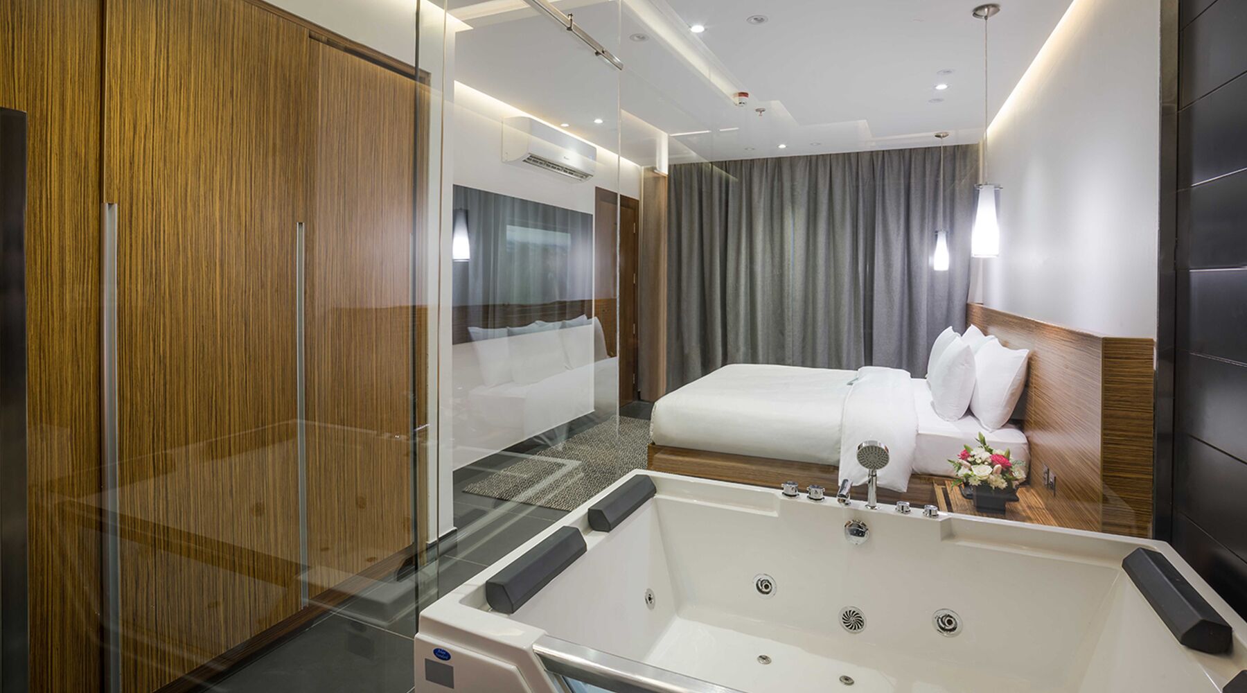 A modern hotel room with a large bed, a glass-enclosed shower, and a wooden wardrobe.