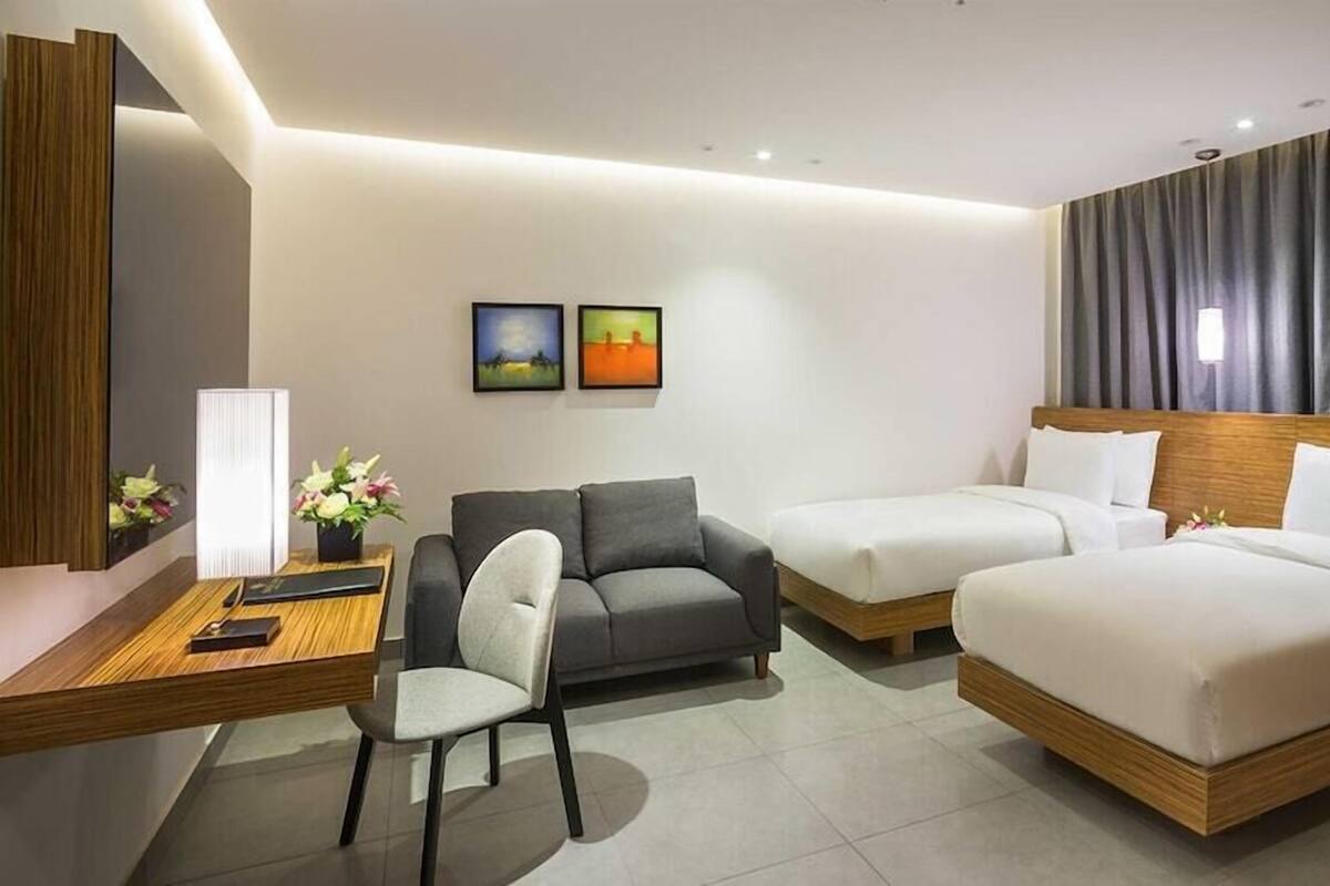 Una habitación de hotel con cama, sofá, escritorio con silla y dos cuadros en la pared.