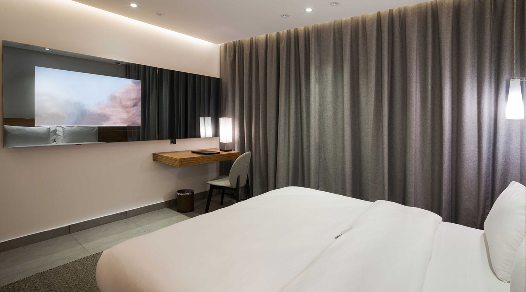 A hotel room with a large bed, a desk with a chair, a television mounted on the wall, and a window with curtains.