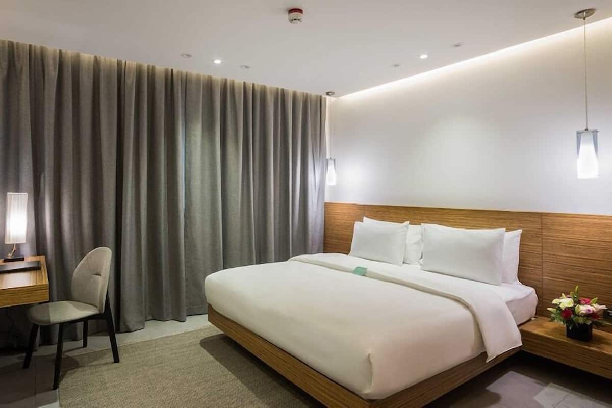 Una habitación de hotel con cama, escritorio, silla y mesita de noche con un florero.