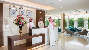 A modern reception area with marble counters, framed portraits, and a large floral arrangement. - Boudl Al Wadi (Riyadh)