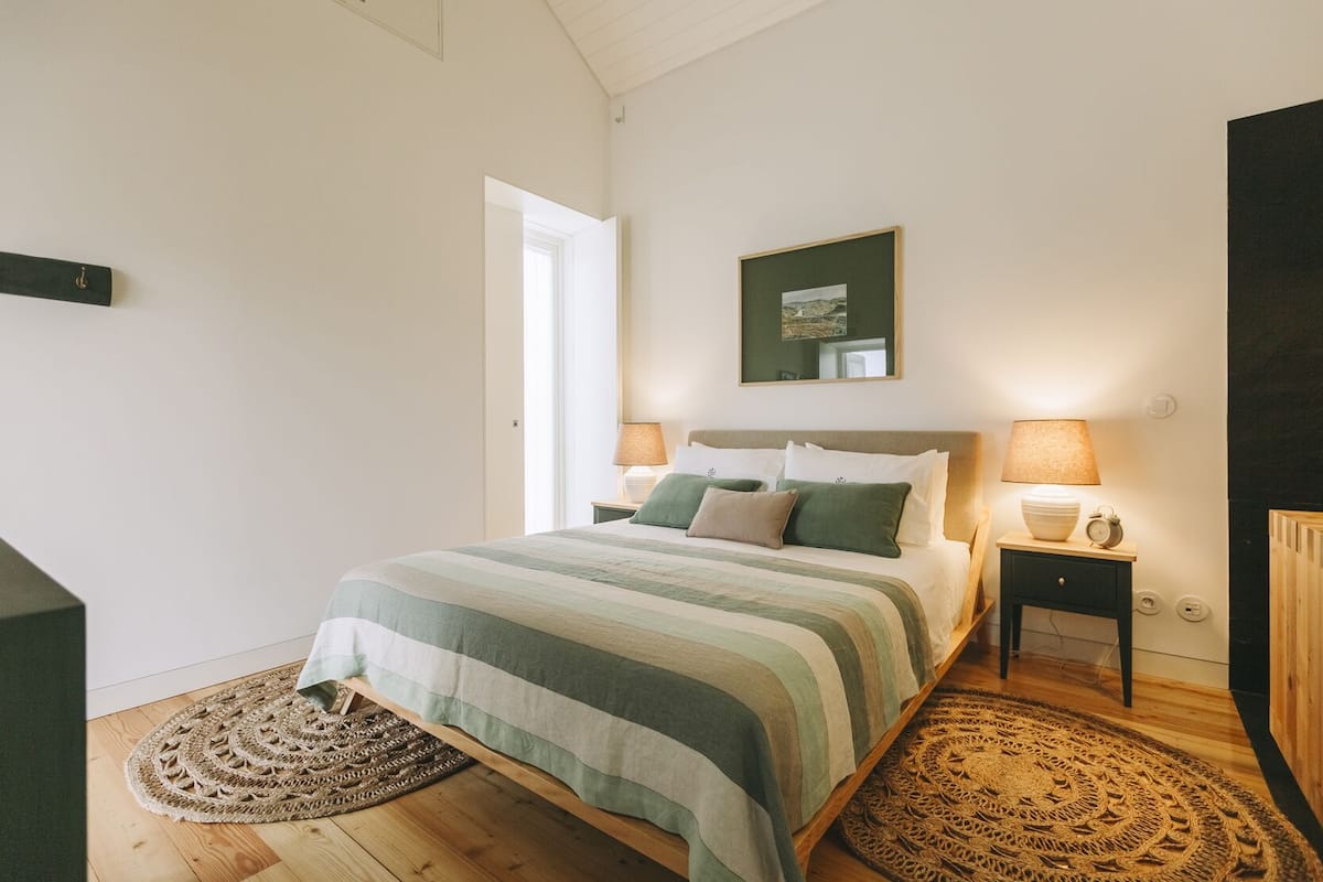 Un dormitorio con una cama, dos mesitas de noche, un cuadro en la pared y una puerta.