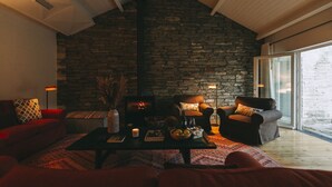 Una sala de estar acogedora con una pared de piedra, dos sofás, una mesa de centro con libros y una vela, y una chimenea.
