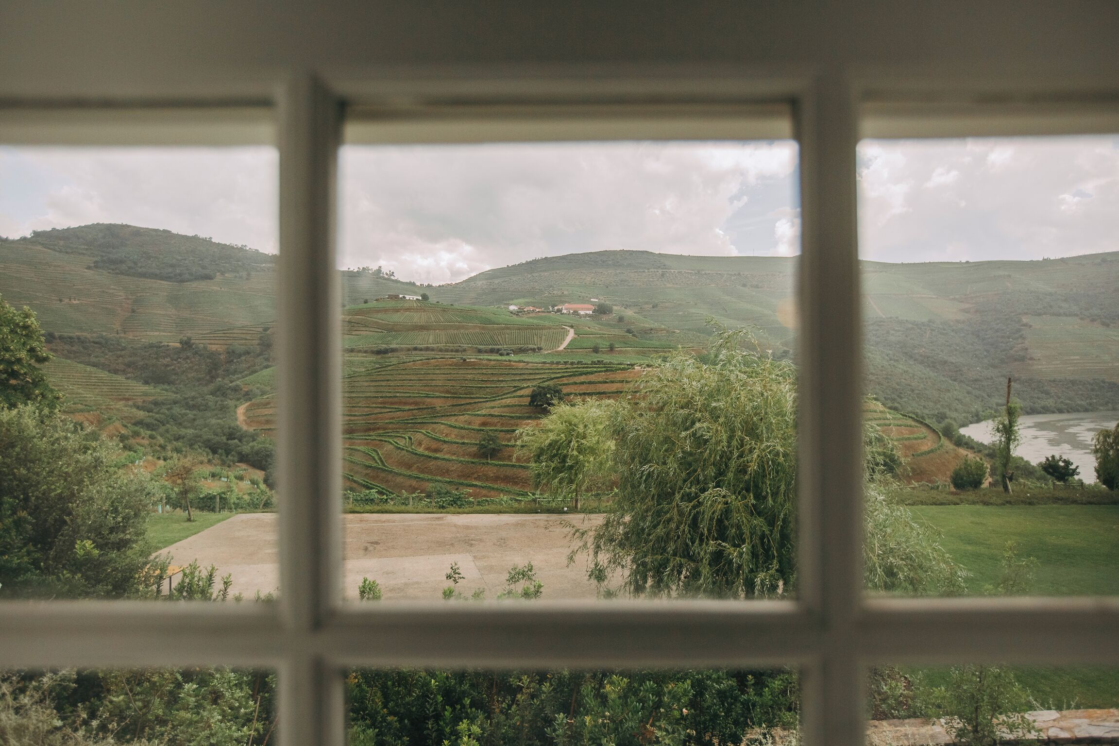 A view through a window of terraced fields and a river, with a building in the distance.