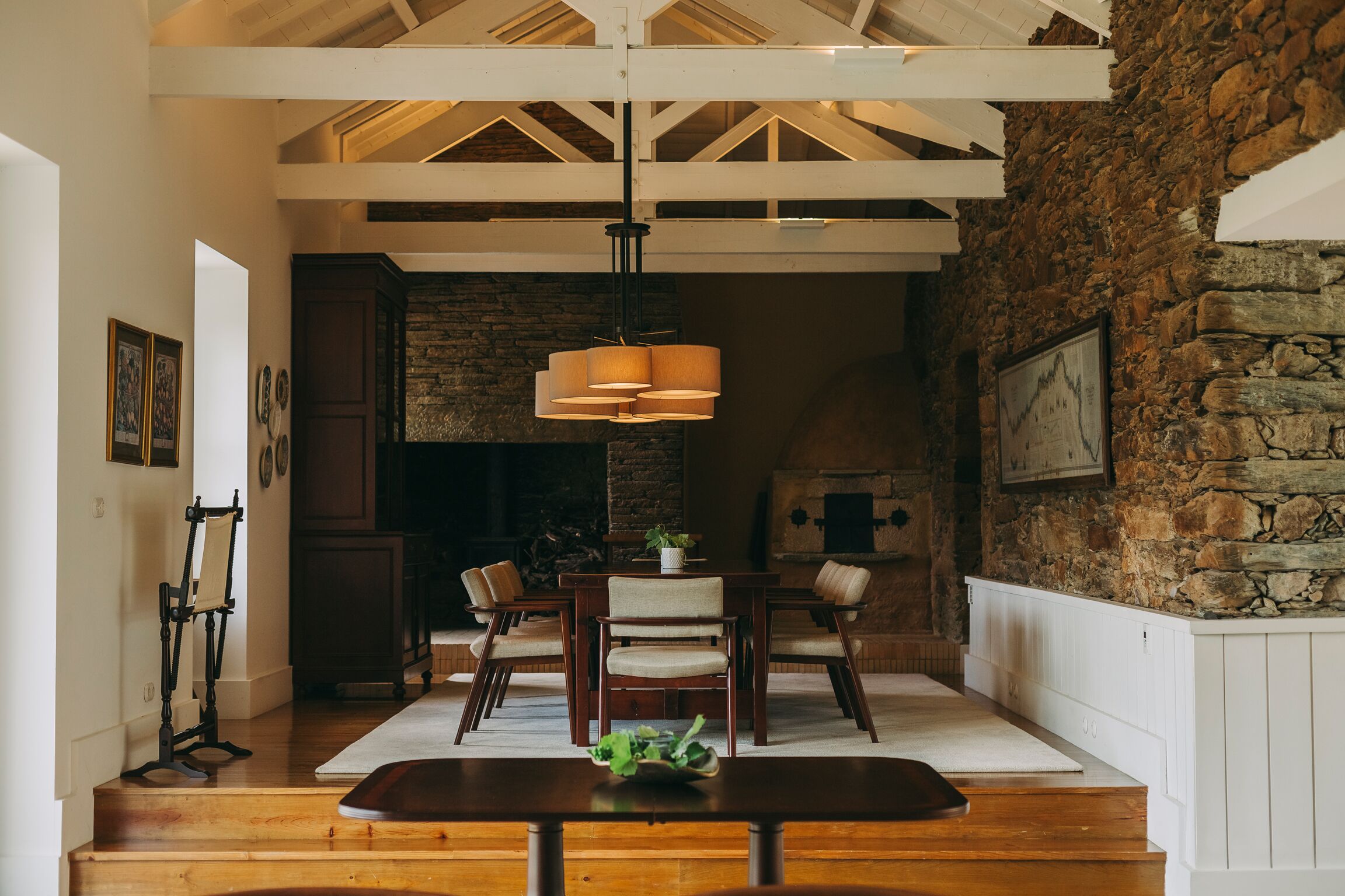 Uma área de refeições com mesa e cadeiras de madeira, luminária pendente e parede de pedra.