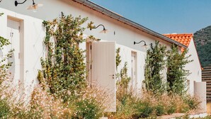 Un edificio blanco con varias puertas y ventanas, rodeado de follaje y plantas.