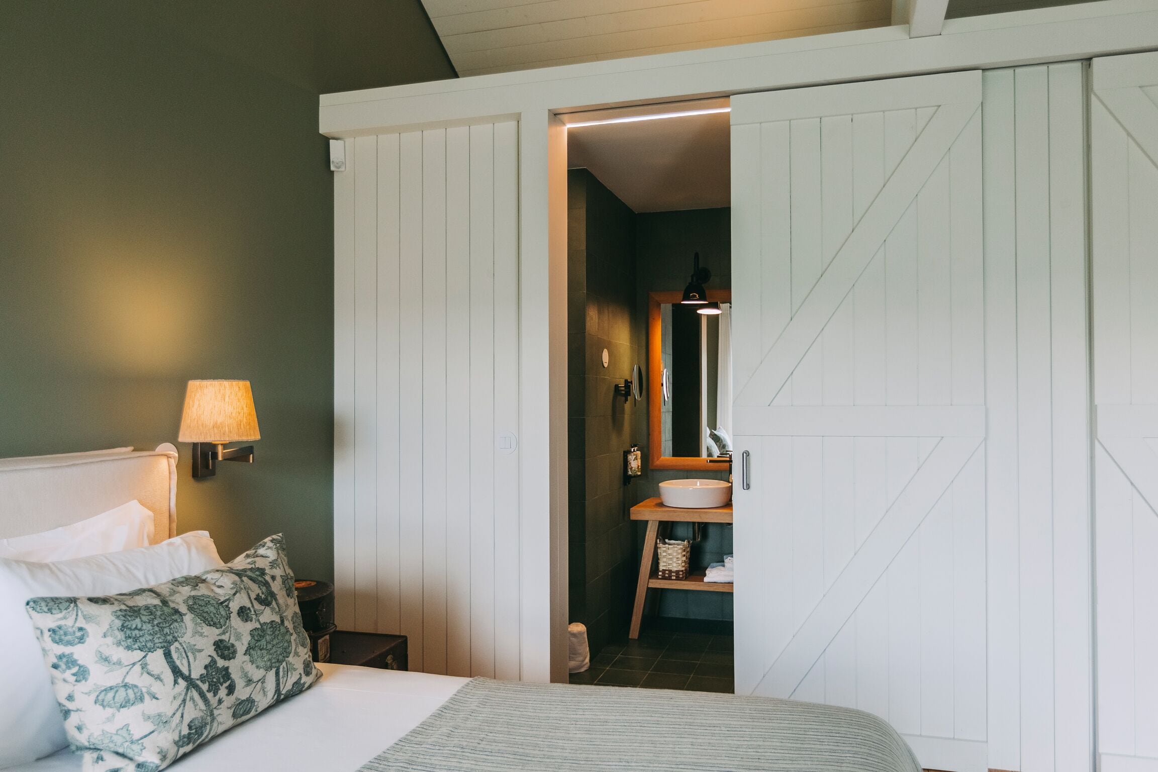 A bedroom with a bed, a nightstand, a lamp, a pillow, and a wardrobe.