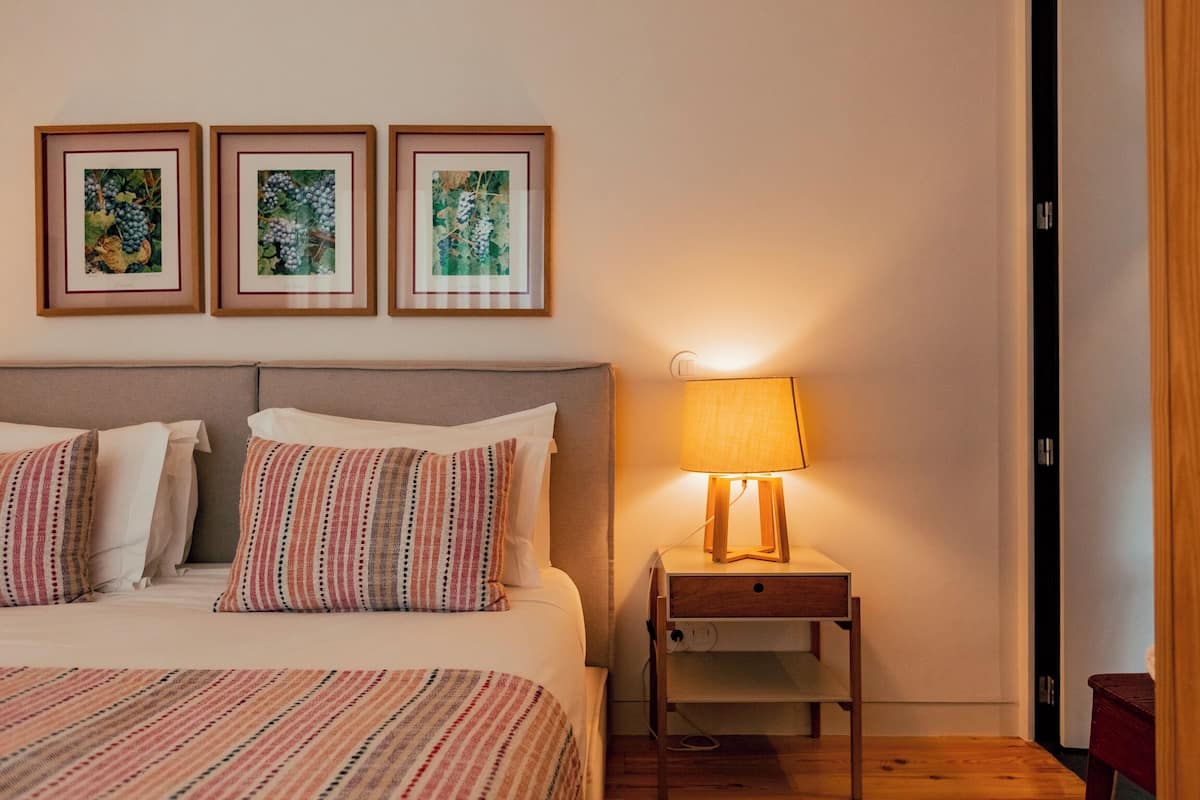 Habitación de hotel con cama, almohadas, mesita de noche con lámpara y tres cuadros en la pared.
