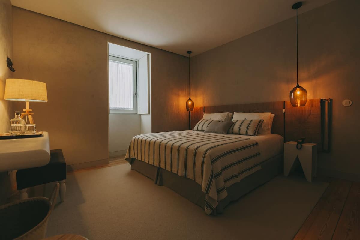 Un dormitorio con cama, mesitas de noche, lámpara y ventana.