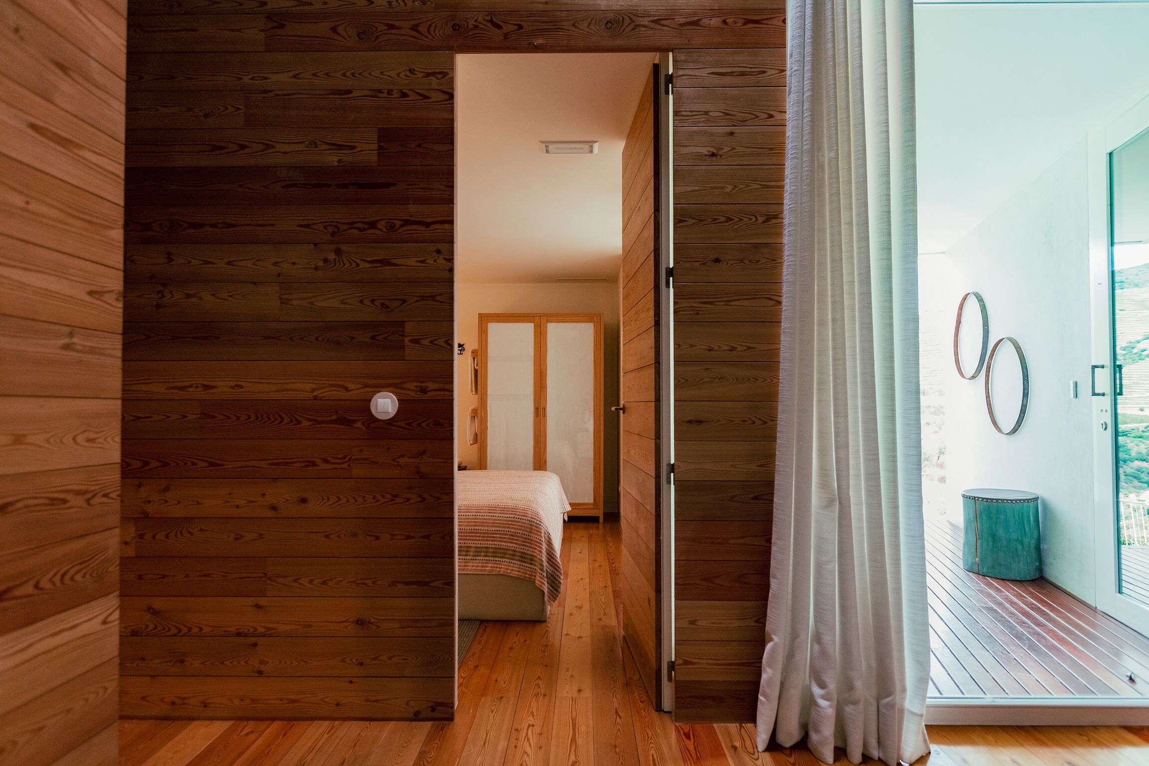 Un intérieur en bois comprenant un lit, une porte coulissante donnant sur un balcon et une vue sur l’extérieur.