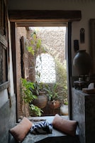 A cozy room with a window, a large potted plant, a rustic wooden door, and a traditional woven basket.