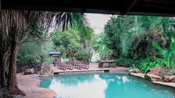 A pool area with lounge chairs and a small pavilion surrounded by lush greenery. - African Heritage House (Mlolongo)