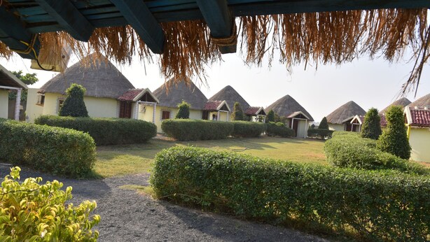 A courtyard with thatched-roof cottages, neatly trimmed hedges, and a gravel path. - Rann Village Resort (Bhuj)