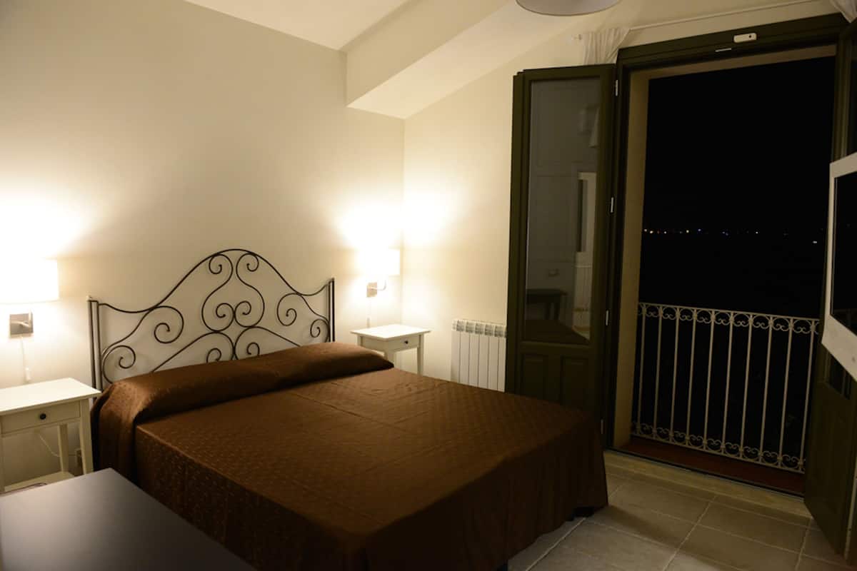A hotel room with a bed, bedside tables, a radiator, and a balcony with a railing.