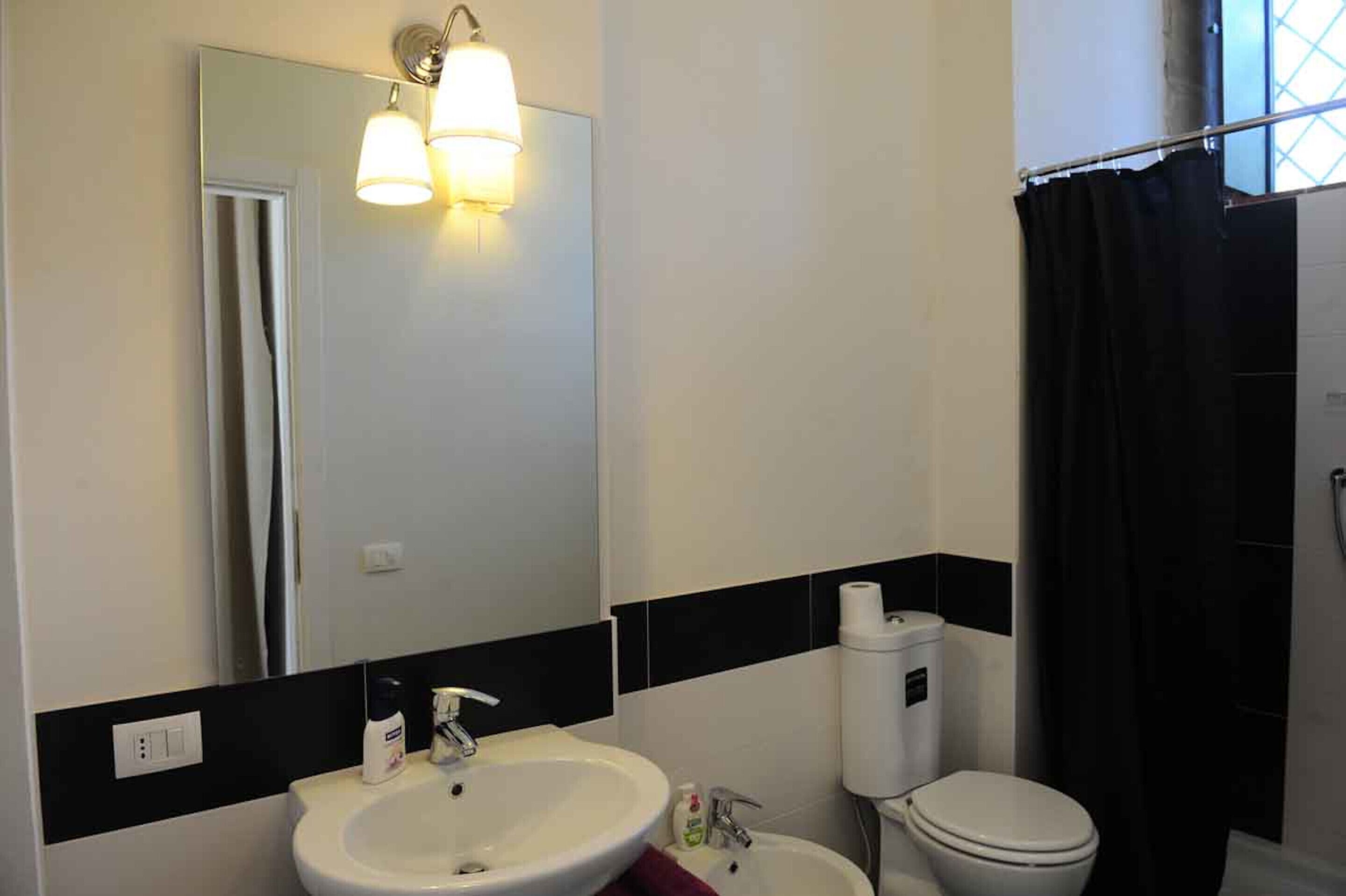 Un baño con un lavamanos blanco, un inodoro, un espejo y una cortina de ducha negra.