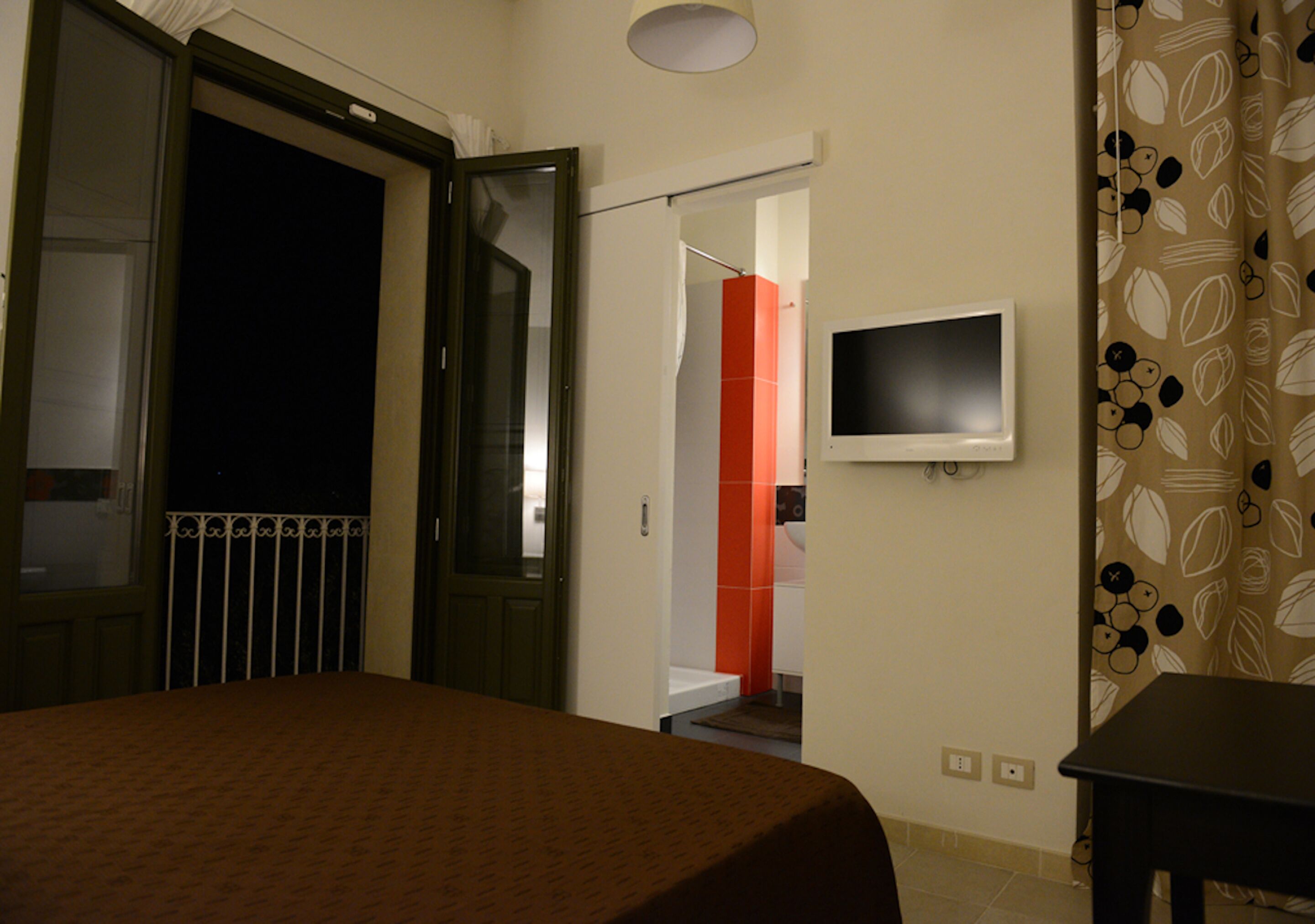 Una camera d'hotel con un letto, una TV fissata al muro e un ingresso che dà su un bagno.