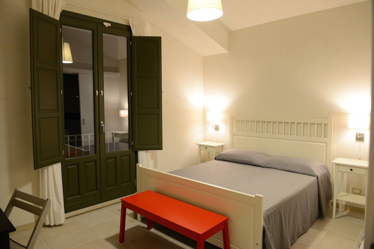 A bedroom with a bed, a bench, a nightstand, and a door with curtains.