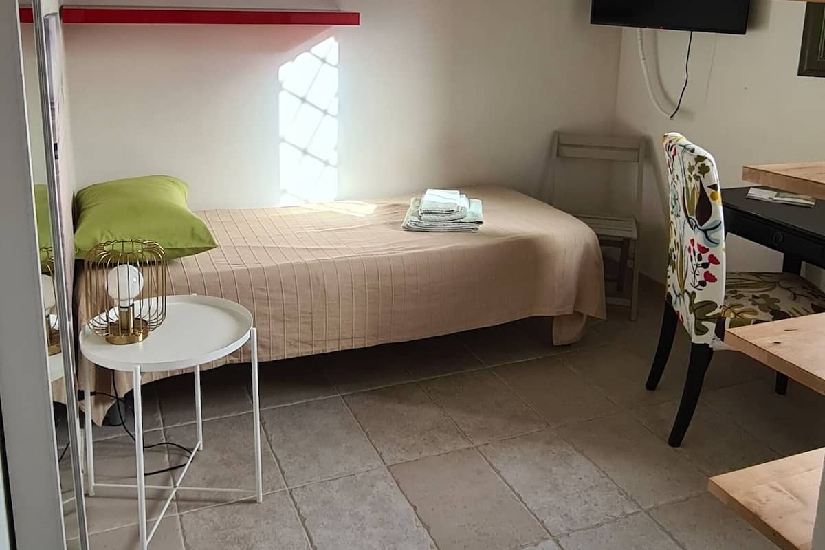 A bedroom with a bed, a desk, a chair, a television, and a window.