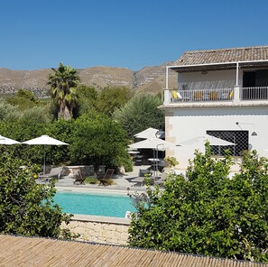 A pool area with lounge chairs and umbrellas, surrounded by greenery and a mountain backdrop. - Tenuta Don Paolino (Avola)