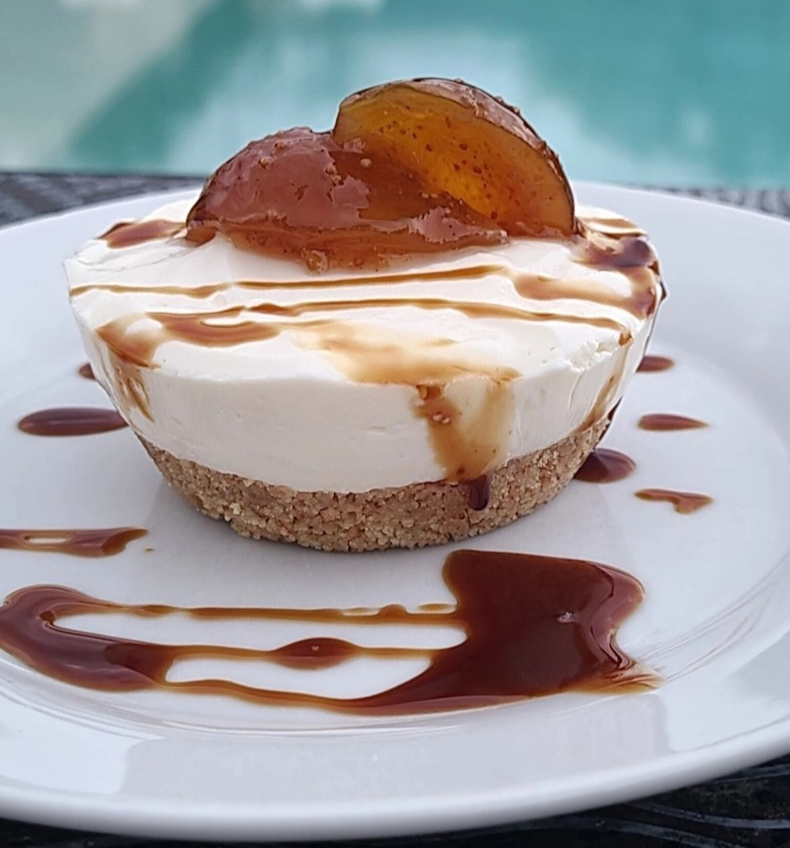 A dessert on a white plate with caramel drizzle and a caramelized fruit on top.