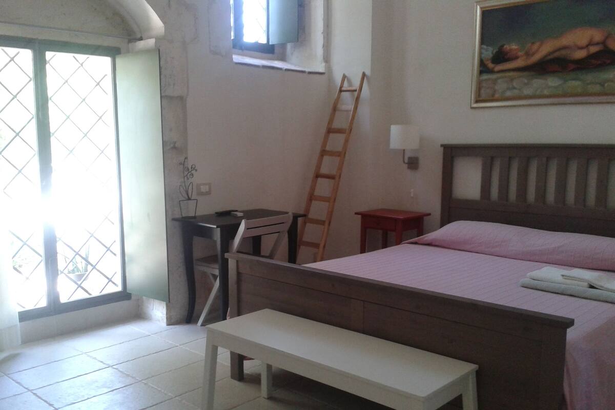 A bedroom with a bed, a desk, a chair, a ladder, and a bench.