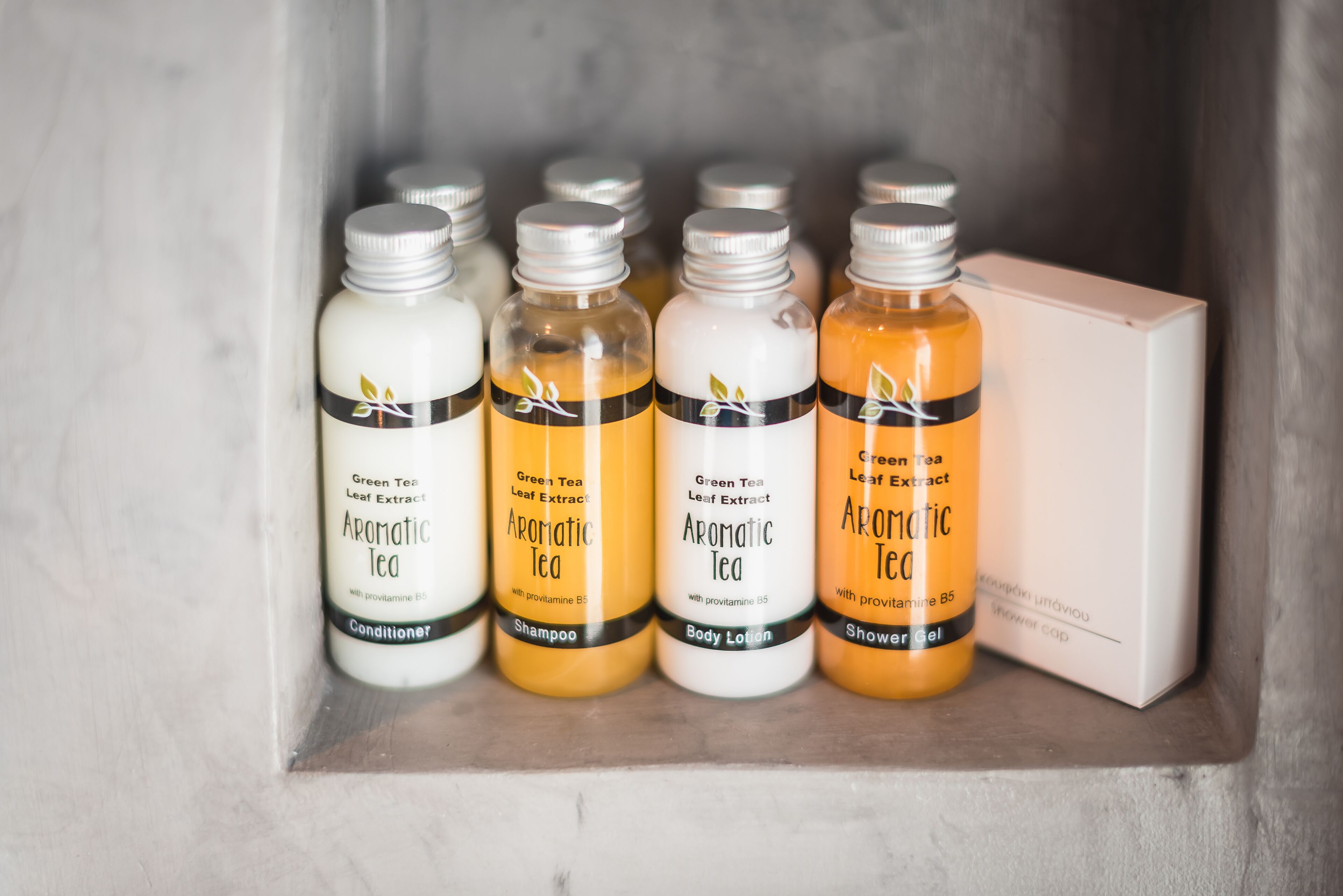 A shelf with various bottles of green tea products, including a conditioner, shampoo, body lotion, and shower gel.