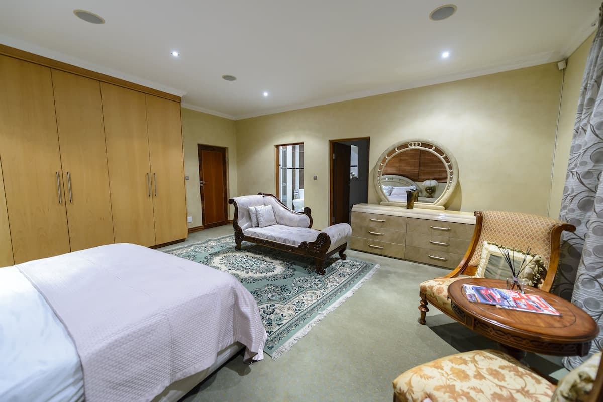A bedroom with a large wardrobe, a bed, a sofa, a round mirror, and a small table.