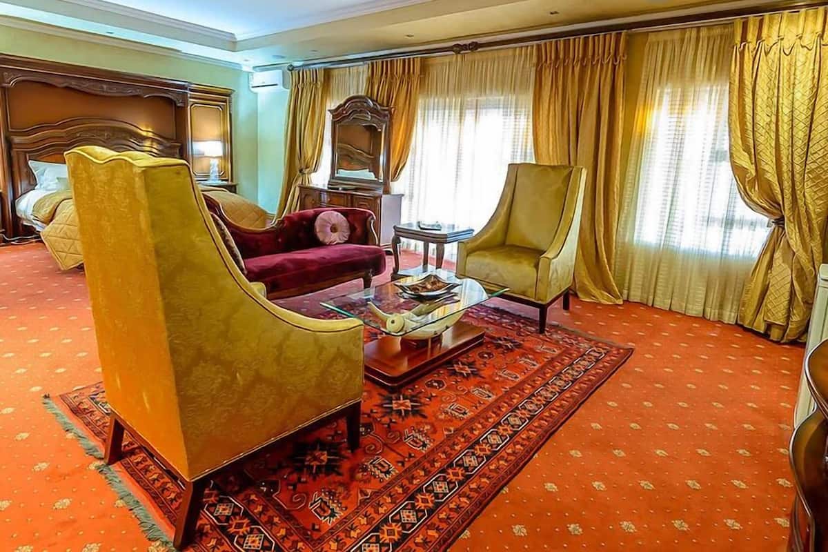 A hotel room with a red carpet, a large armchair, a sofa, a small table with a book, and a mirror.