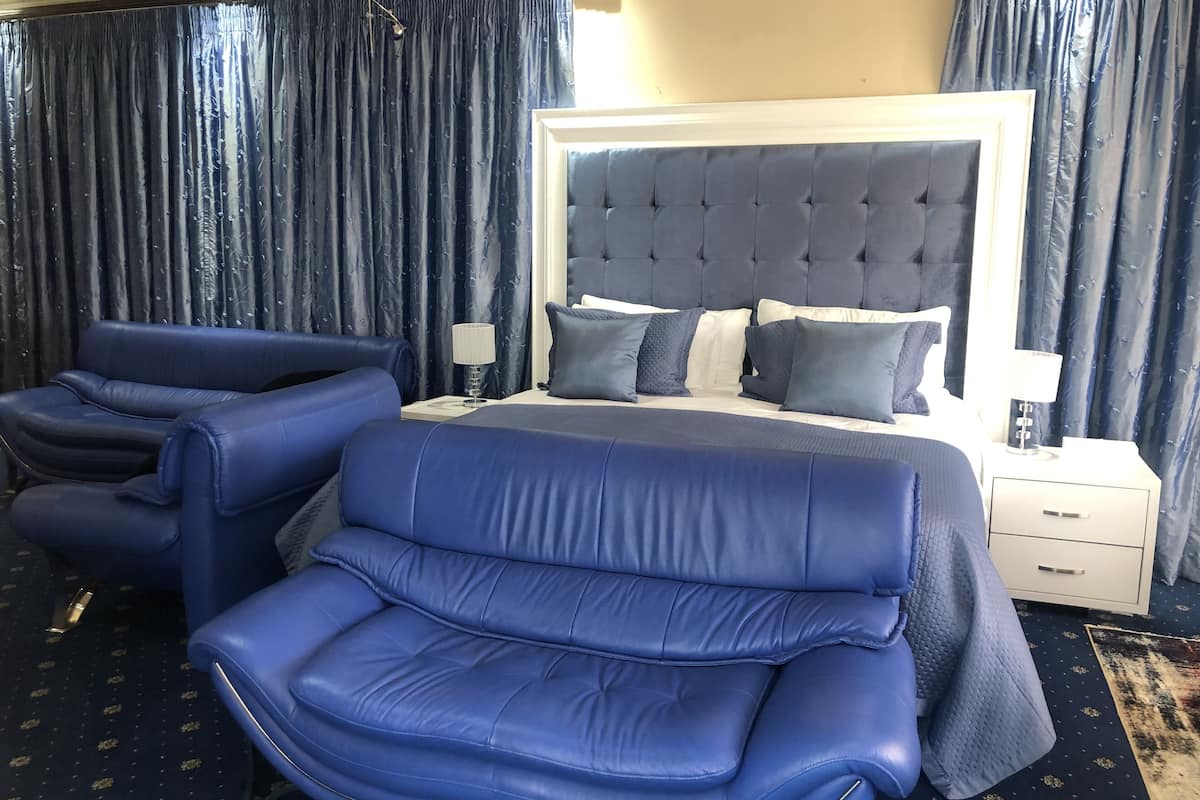 A hotel room with a large bed, two blue sofas, a nightstand with a lamp, and a patterned carpet.