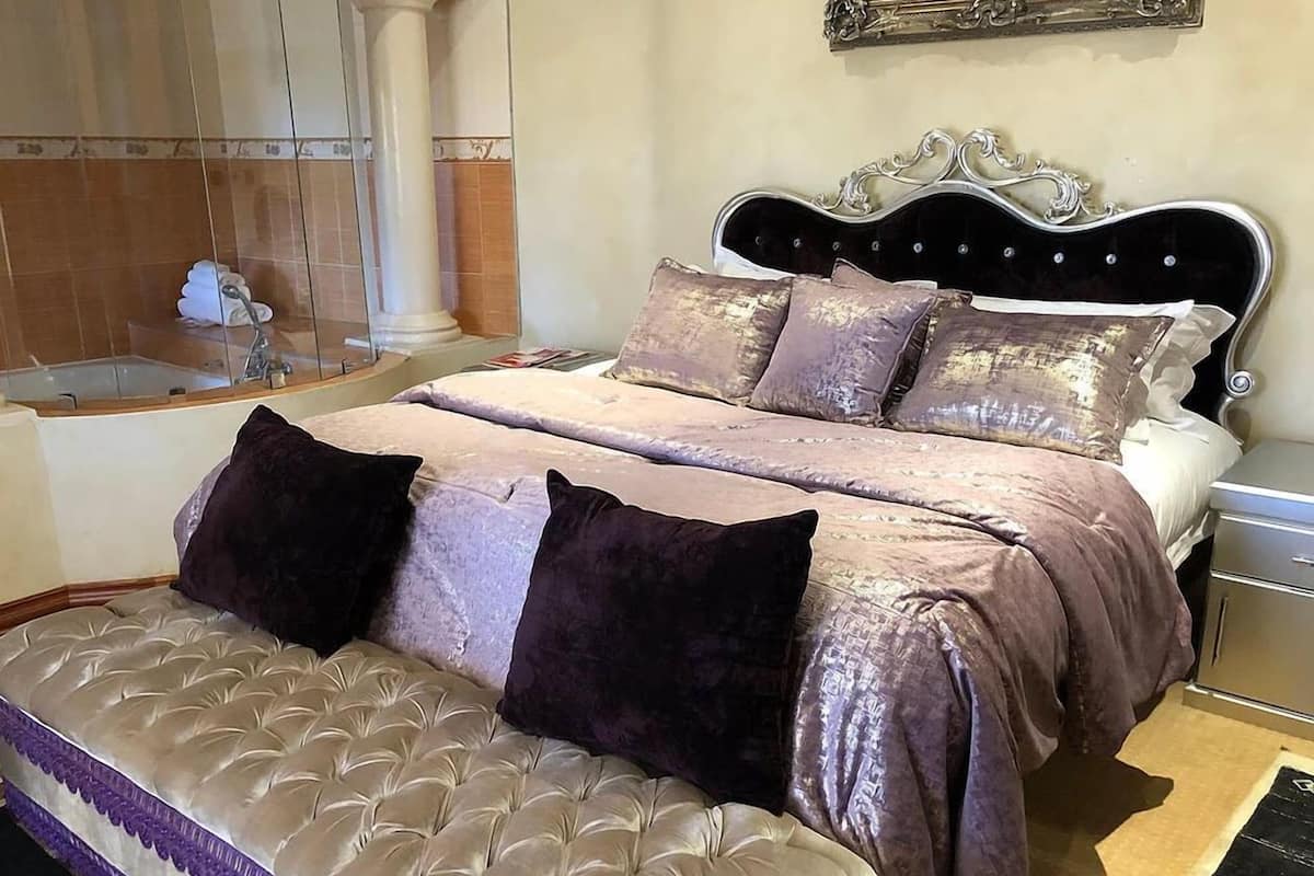 A bedroom with a large bed, a nightstand, a dresser, and a bathroom with a bathtub.