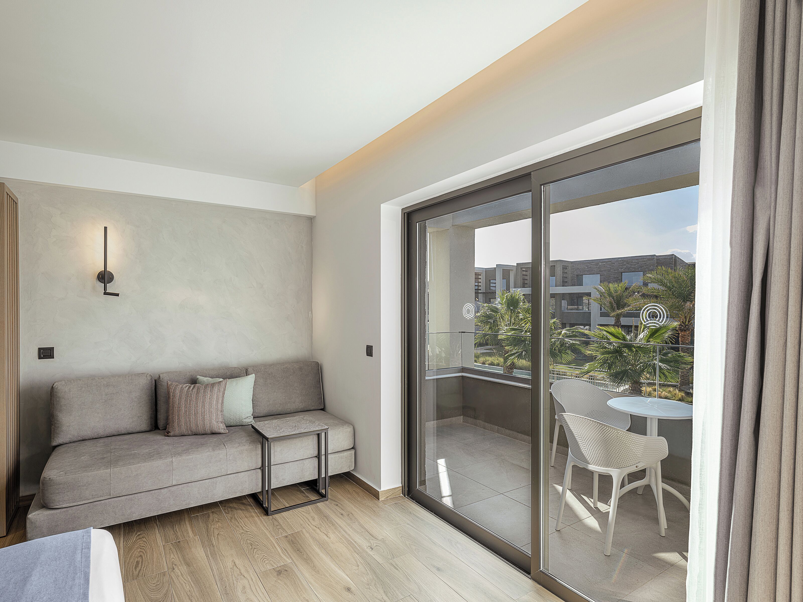 A modern living room with a grey sofa, a small side table, and a balcony with a white chair and table.